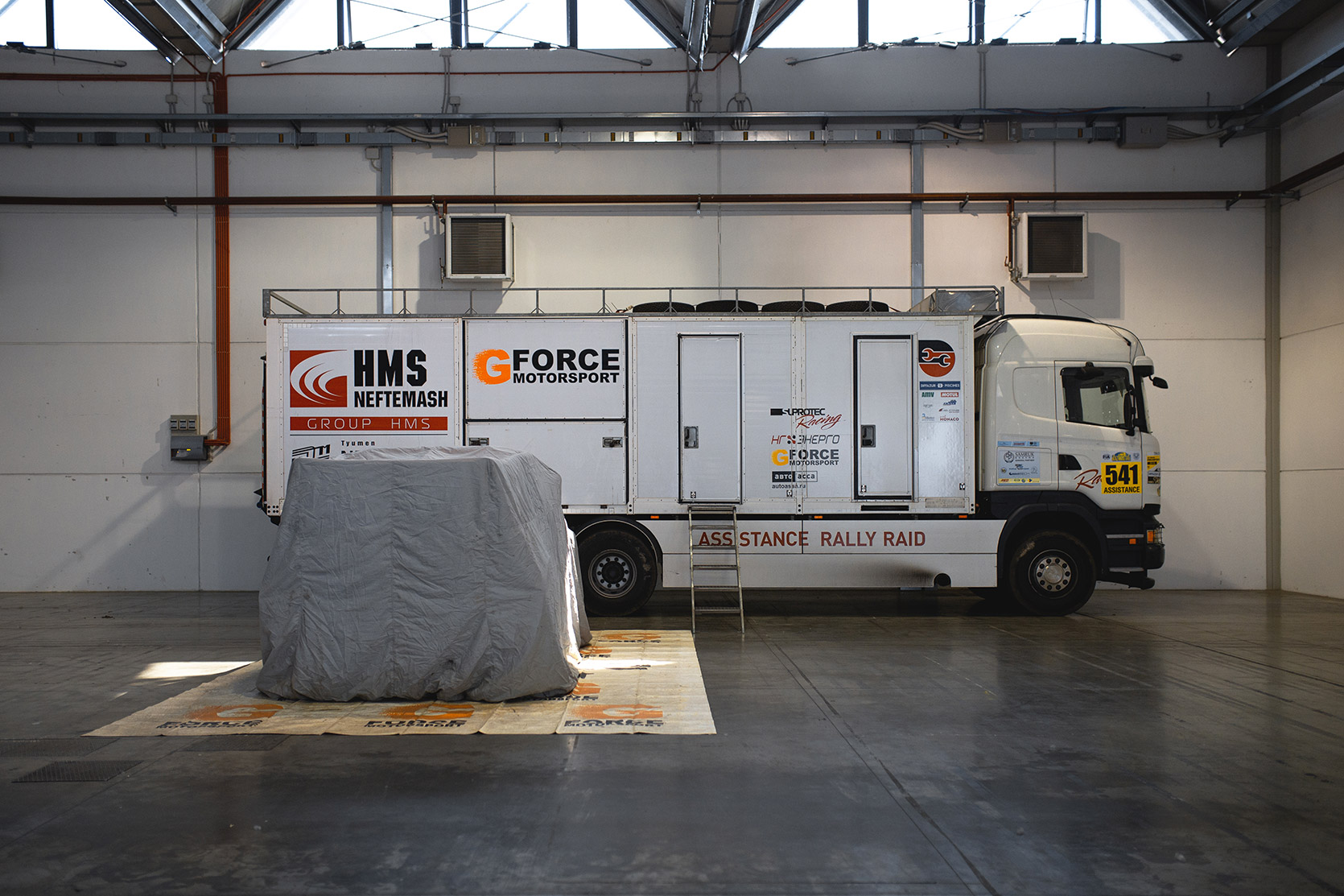 The G-Force Motorsport Truck near a covered car in the paddock at Italian Baja